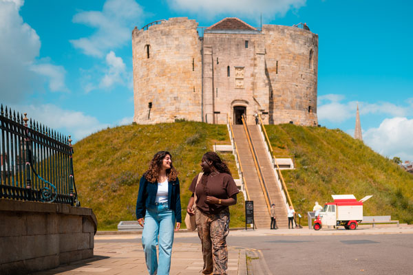 Two students walking past Clifford's Tower in Ƶapp
